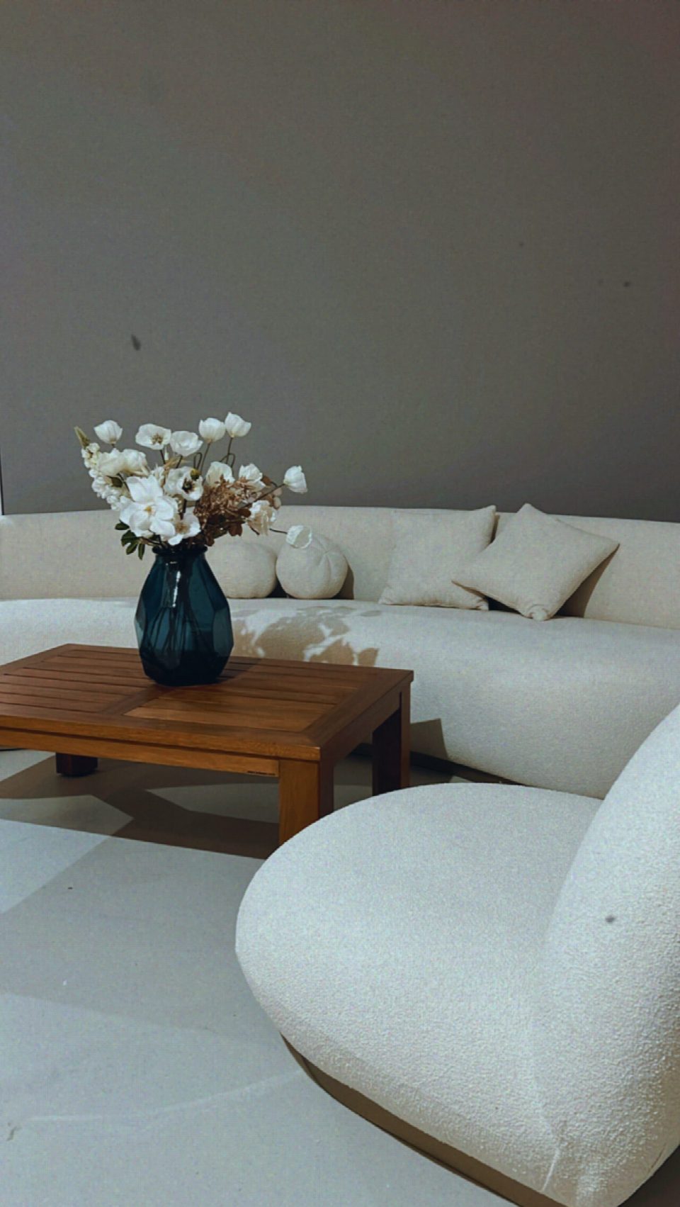 Weißes Bouclé-Sofa mit Holztisch und Blumen